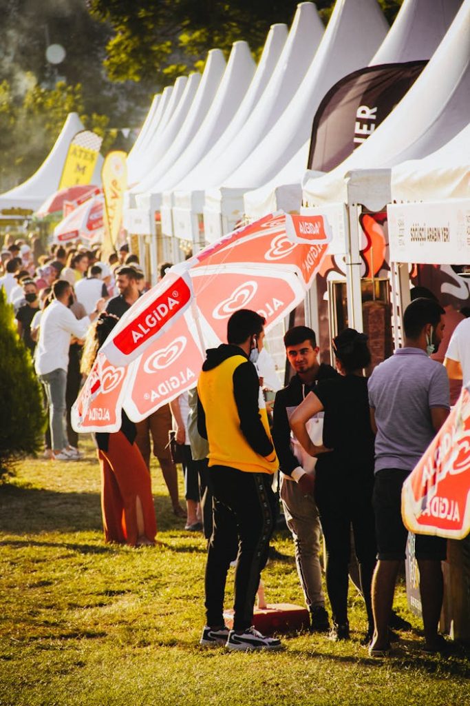 Crowded outdoor festival scene with food stalls and vibrant tents under bright daylight.